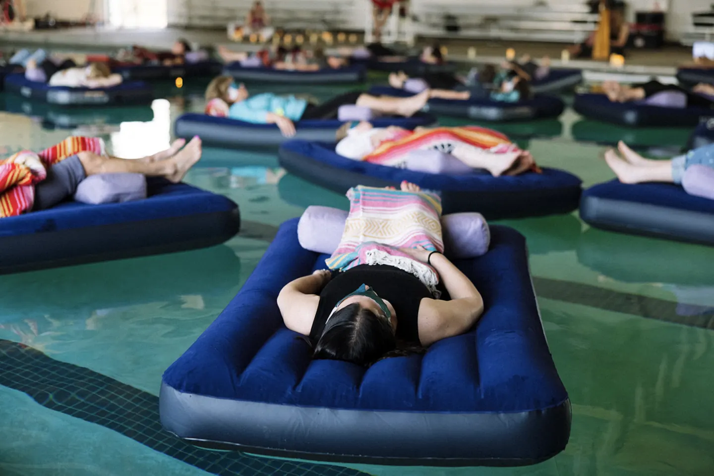 Sound bath participants resting on floating air mattresses in a pool.