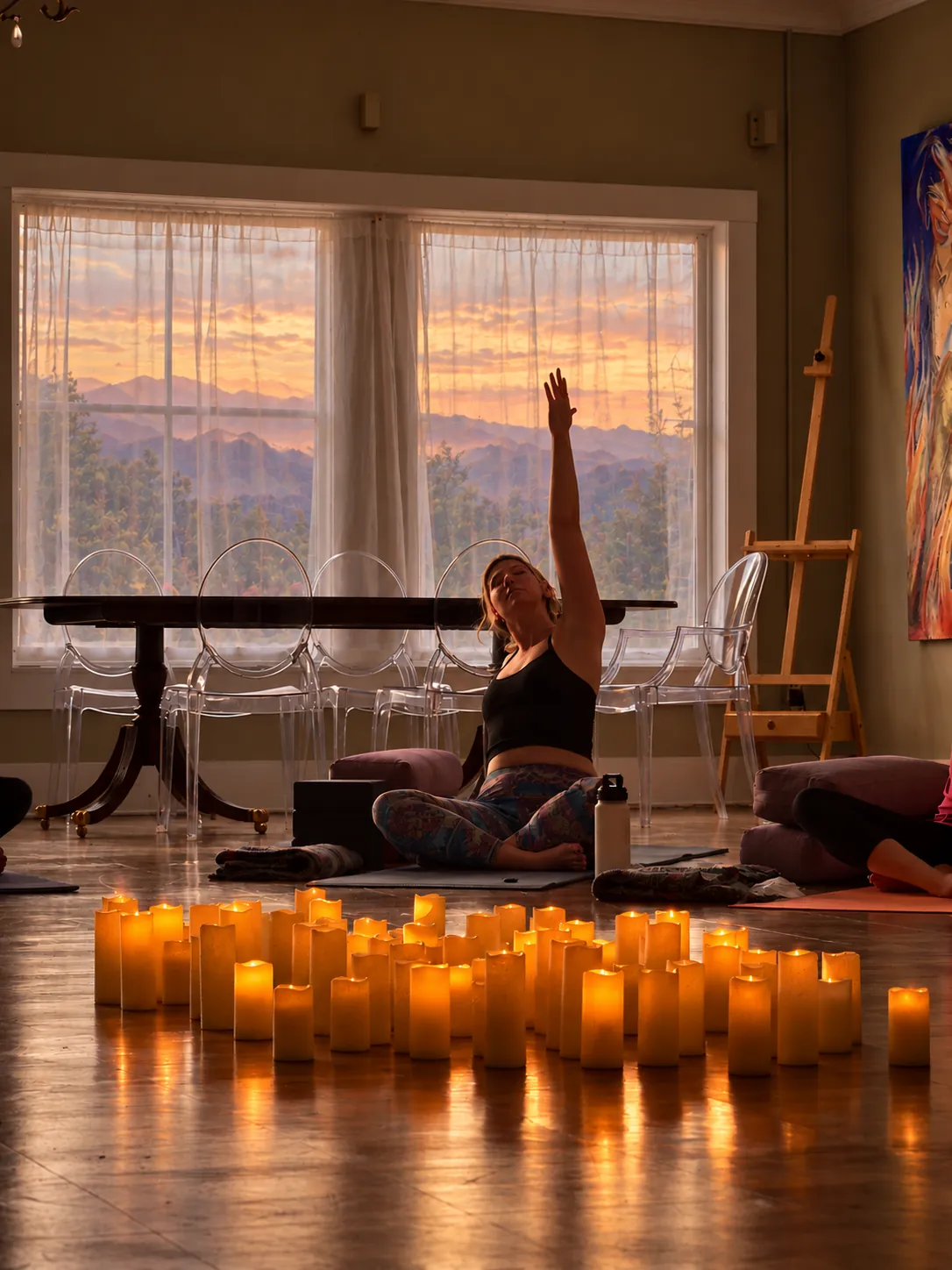 A yoga participant seated by candlelight with a Smoky Mountain sunset through the windows.